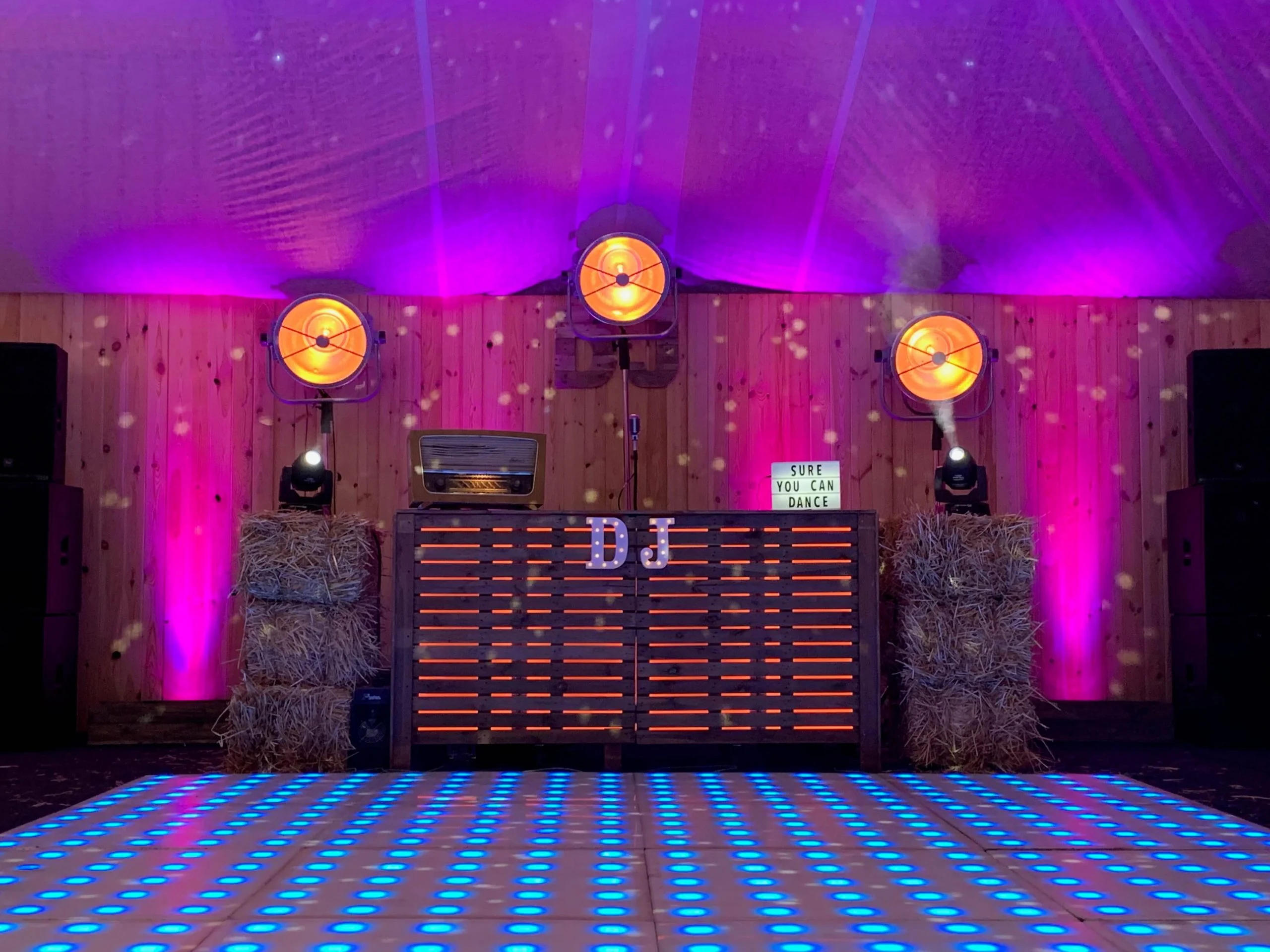 Houten DJ-booth achter een verlichte dansvloer met paarse zaalverlichting